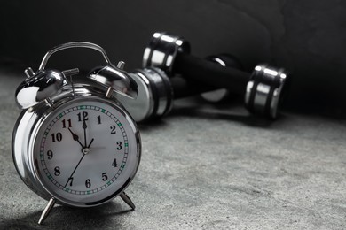 Photo of Alarm clock and dumbbells on grey background