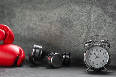 Photo of Alarm clock, boxing gloves and dumbbells on grey background. Space for text