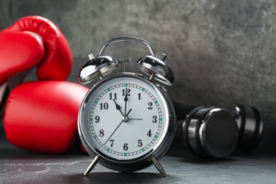 Photo of Alarm clock, boxing gloves and dumbbells on grey background