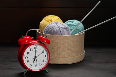 Photo of Alarm clock, yarn and knitting needles on wooden background