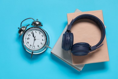 Photo of Alarm clock, books and headphones on light blue background