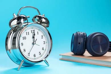 Photo of Alarm clock, book and headphones on light blue background