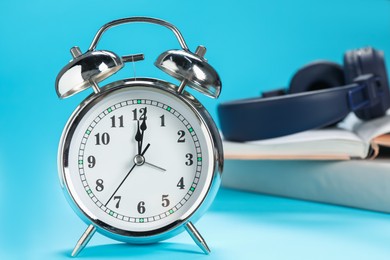 Photo of Alarm clock, books and headphones on light blue background