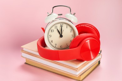 Photo of Alarm clock, books and headphones on light pink background