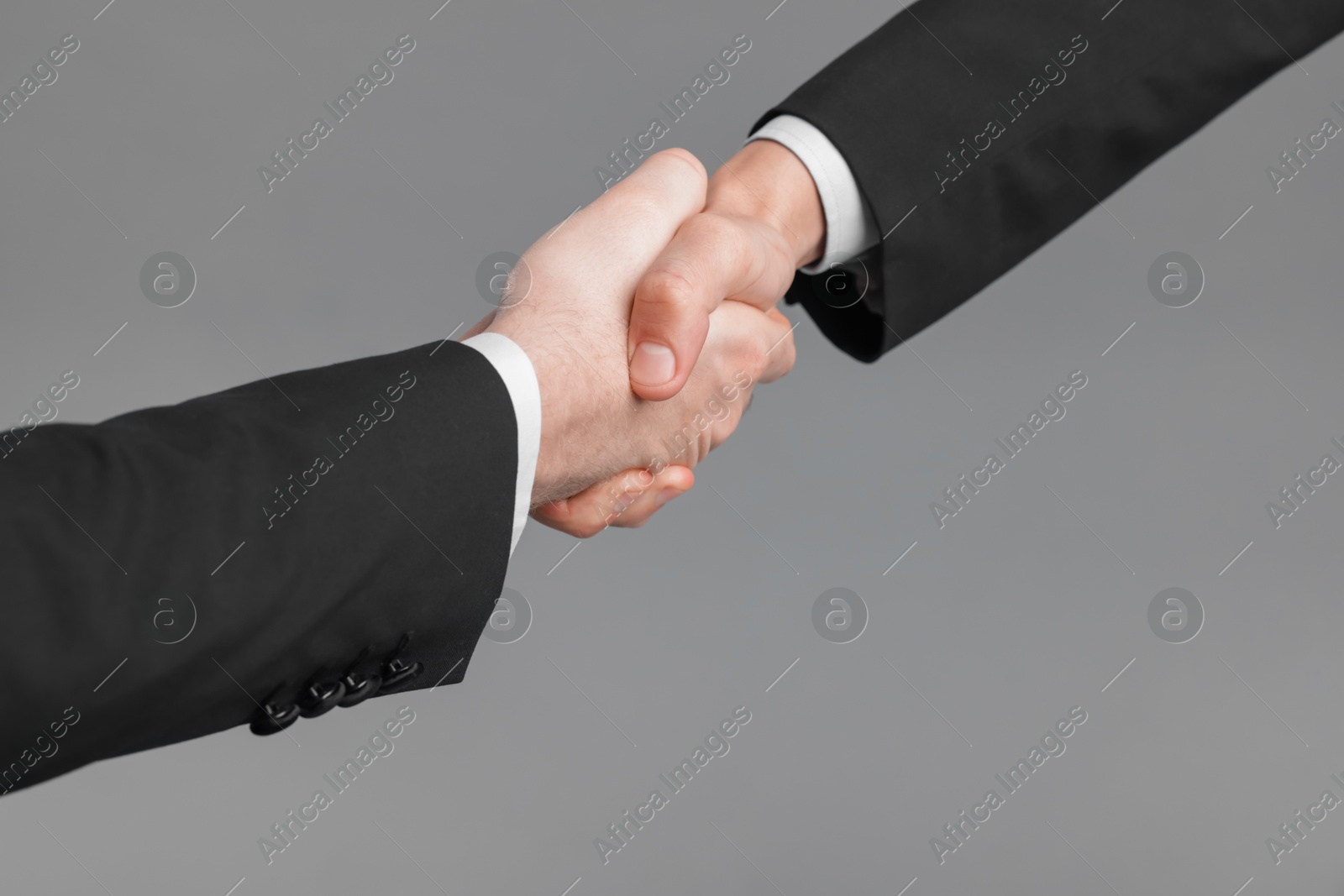 Photo of Businessmen shaking hands on grey background, closeup