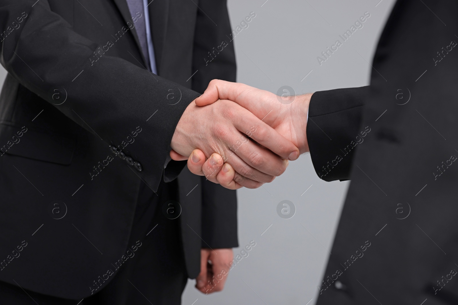 Photo of Businessmen shaking hands on grey background, closeup