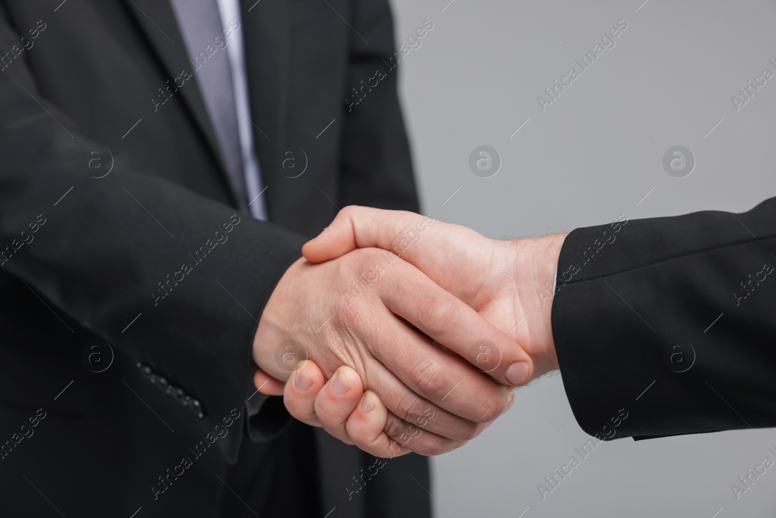 Photo of Businessmen shaking hands on grey background, closeup