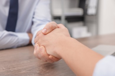 Businessmen shaking hands at wooden desk in office, closeup