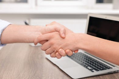 Businessmen shaking hands at wooden desk in office, closeup