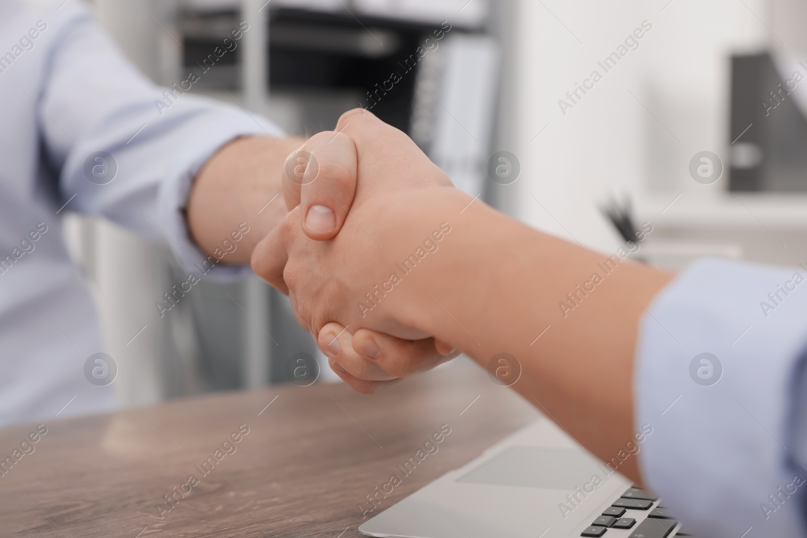 Photo of Businessmen shaking hands at wooden desk in office, closeup