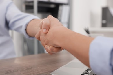 Photo of Businessmen shaking hands at wooden desk in office, closeup