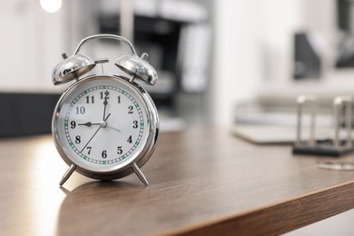 Photo of Alarm clock on wooden desk in office. Space for text