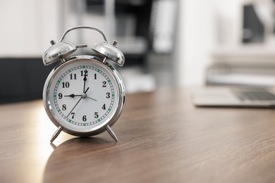 Photo of Alarm clock on wooden desk in office. Space for text