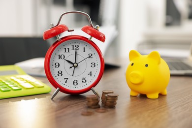 Photo of Alarm clock, piggybank and coins on wooden desk in office