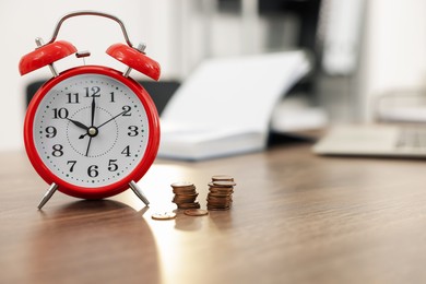 Photo of Alarm clock and coins on wooden desk in office. Space for text