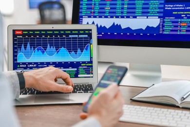 Photo of Financial trading specialist with smartphone and laptop at table in office, closeup