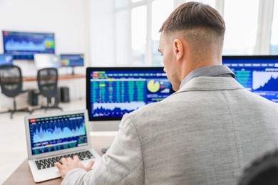 Financial trading specialist working on laptop and computer in office, back view