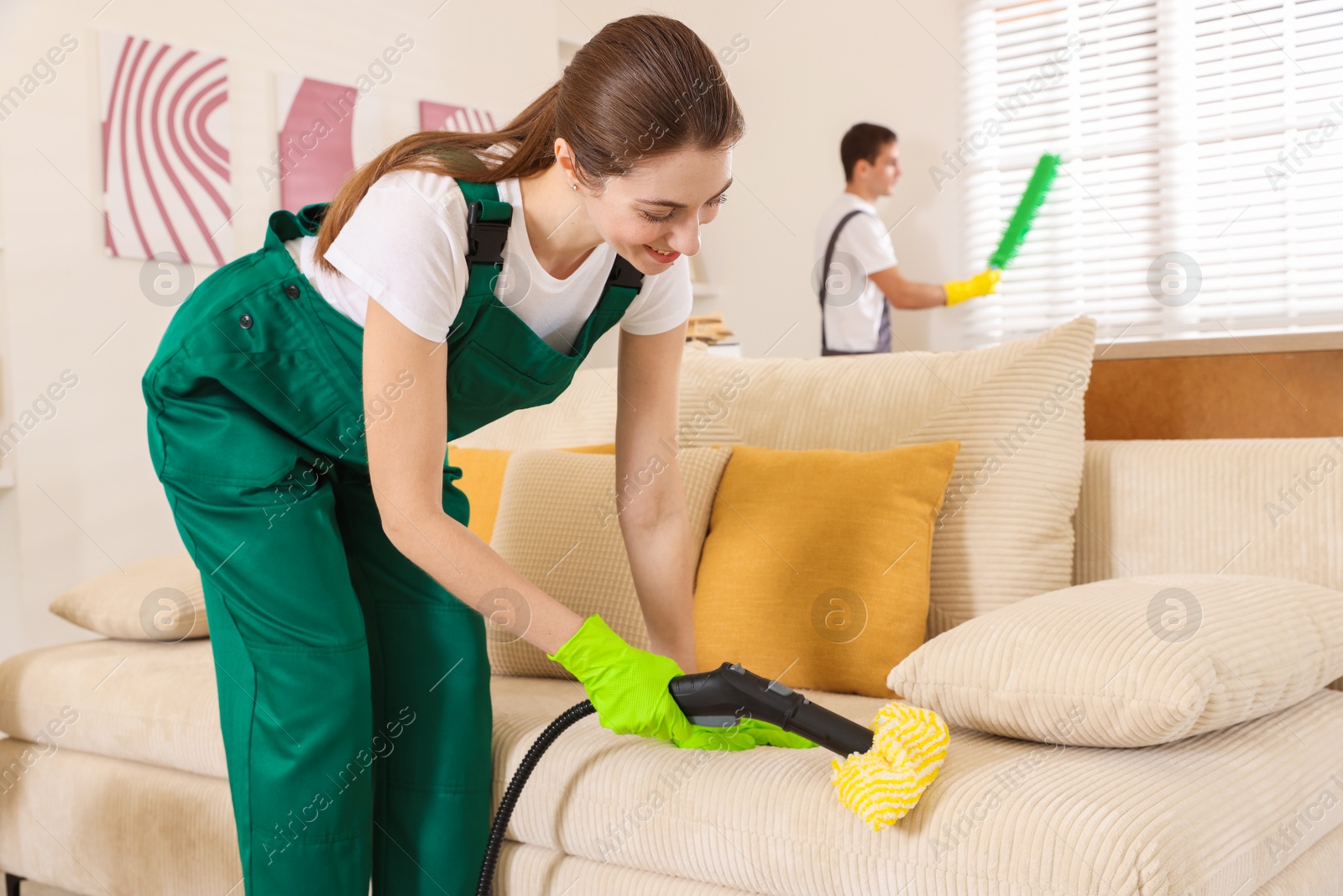 Photo of Professional janitor steam cleaning sofa in room