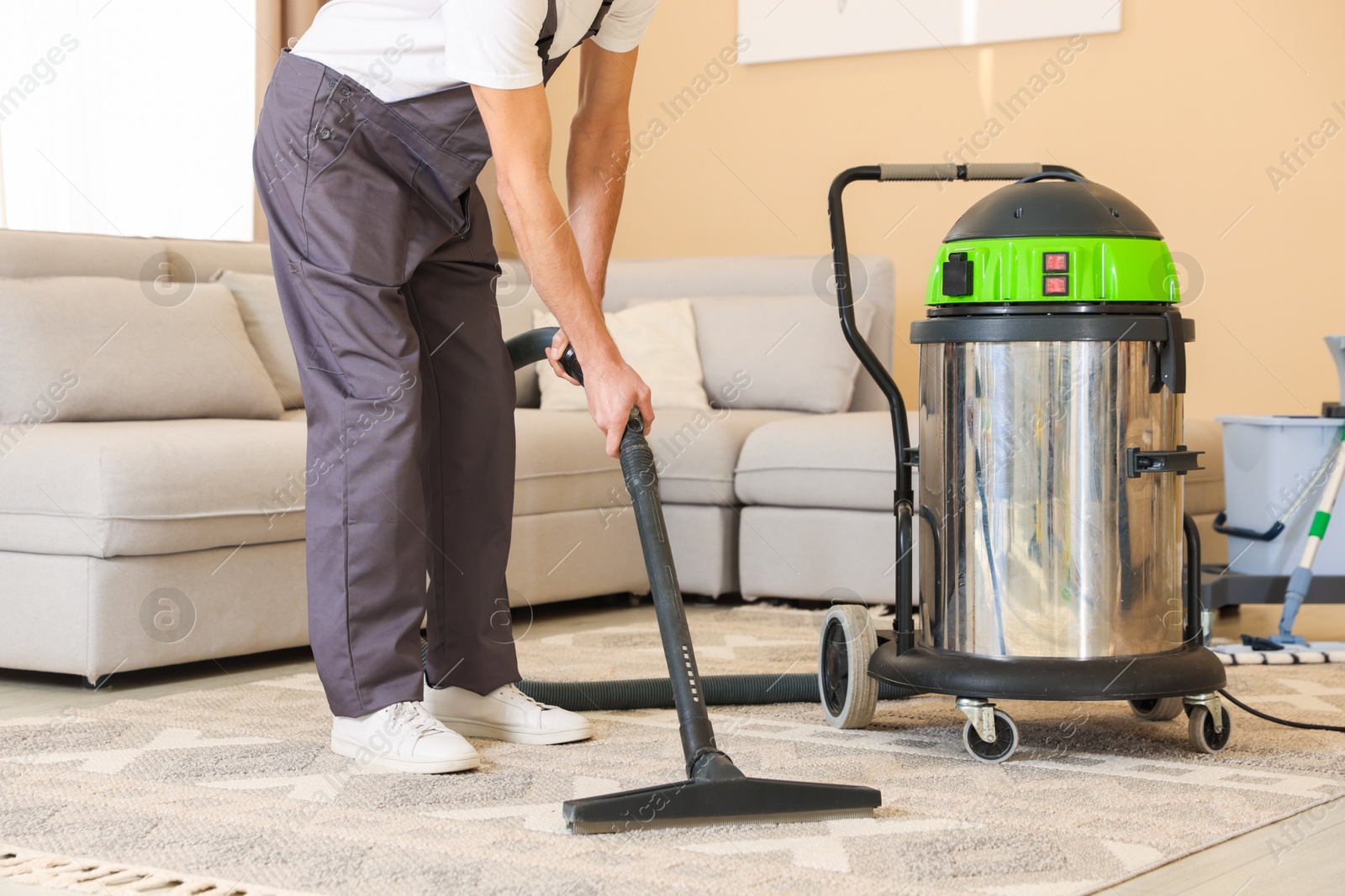 Photo of Professional cleaning service worker vacuuming rug indoors, closeup