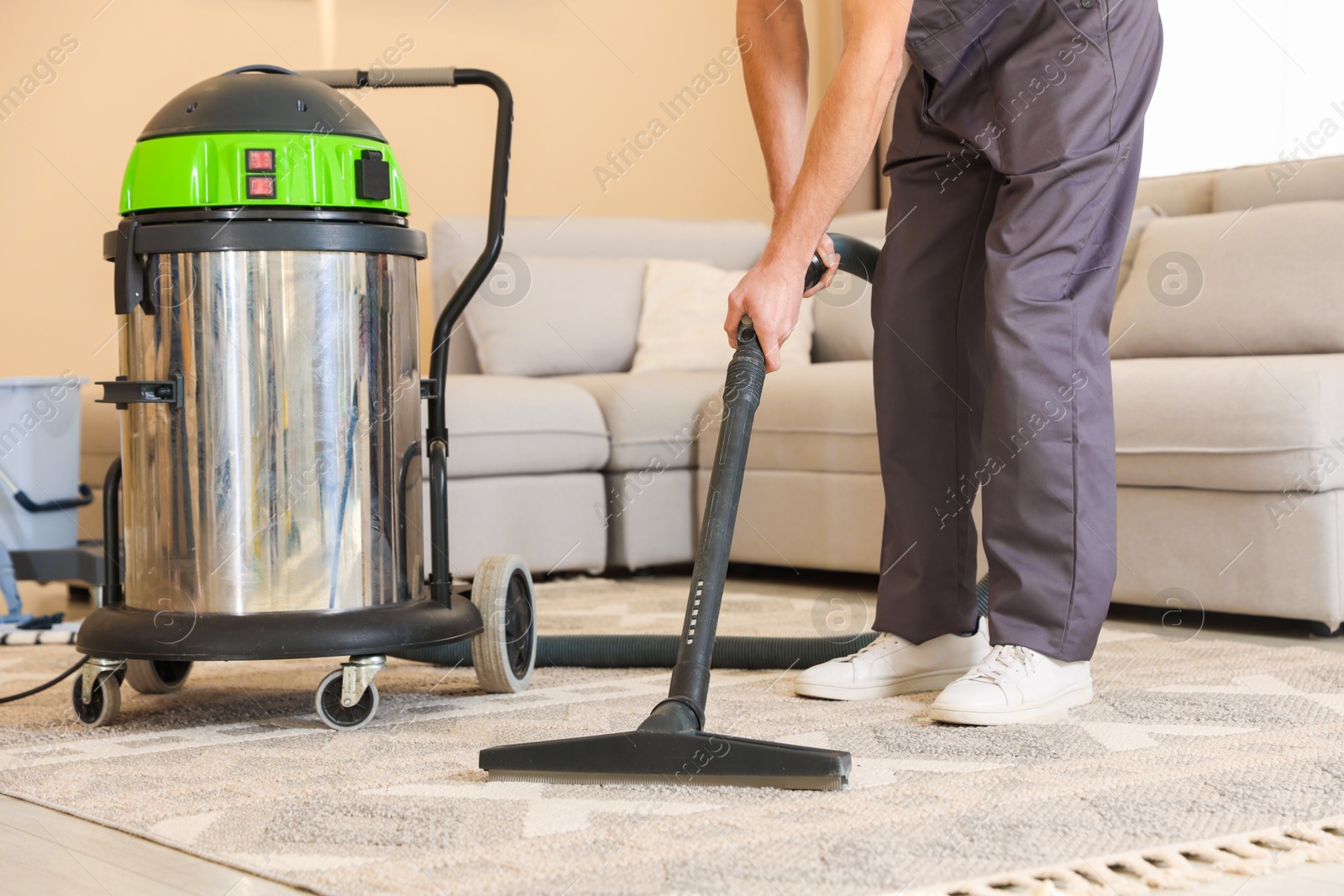 Photo of Professional cleaning service worker vacuuming rug indoors, closeup