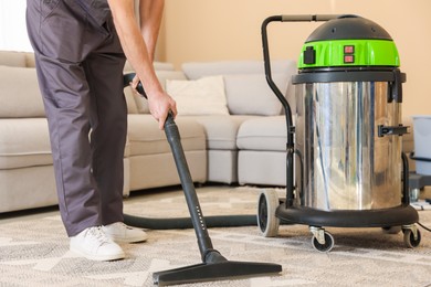 Professional cleaning service worker vacuuming rug indoors, closeup