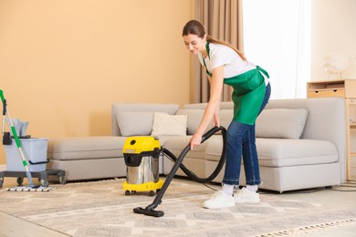 Photo of Professional cleaning service worker vacuuming rug indoors