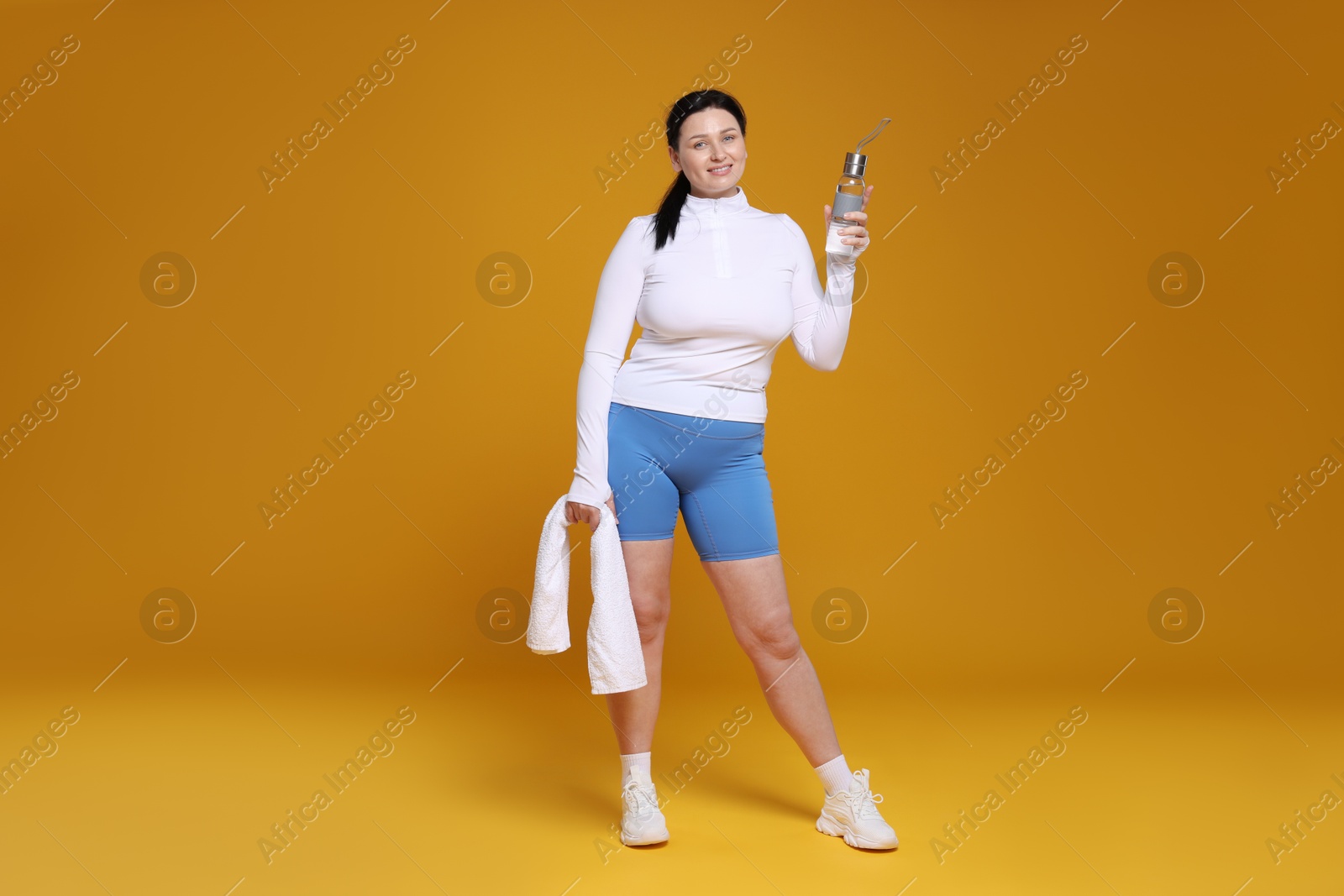 Photo of Plus size woman in gym clothes with water bottle and towel on orange background