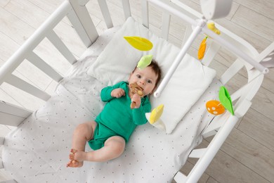 Photo of Cute little baby in crib with cot mobile at home, above view