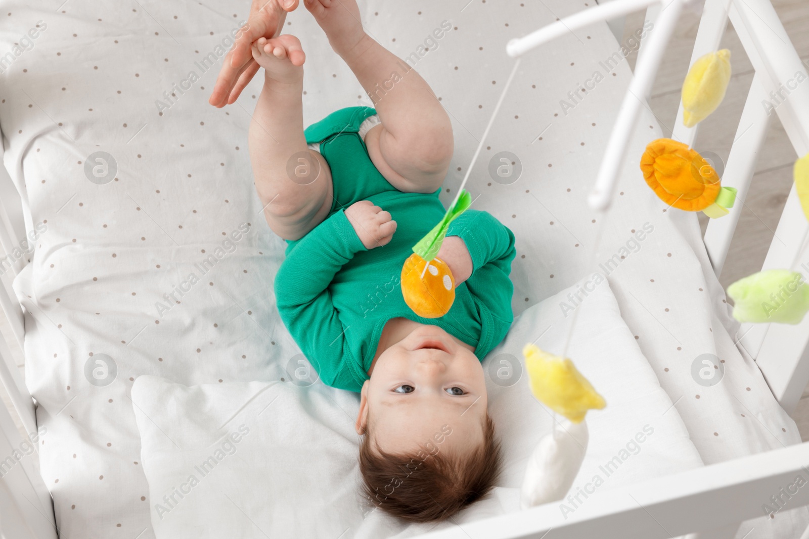 Photo of Cute little baby playing with cot mobile in crib at home