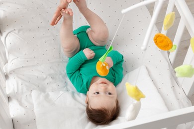 Photo of Cute little baby playing with cot mobile in crib at home