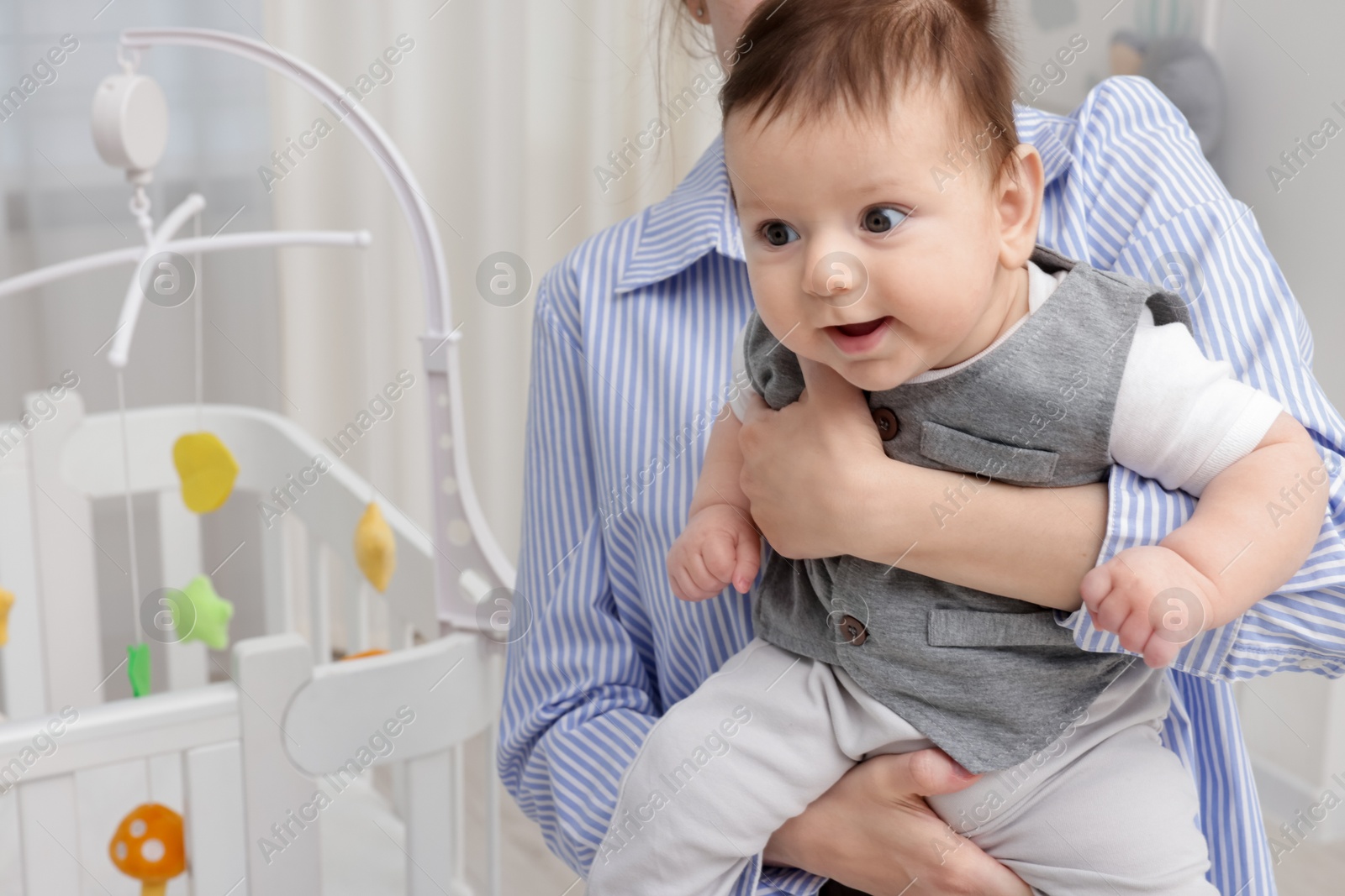 Photo of Mother holding her little baby, closeup. Crib with cot mobile in nursery