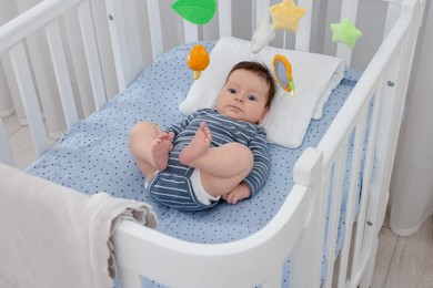 Photo of Cute little baby in crib with cot mobile at home