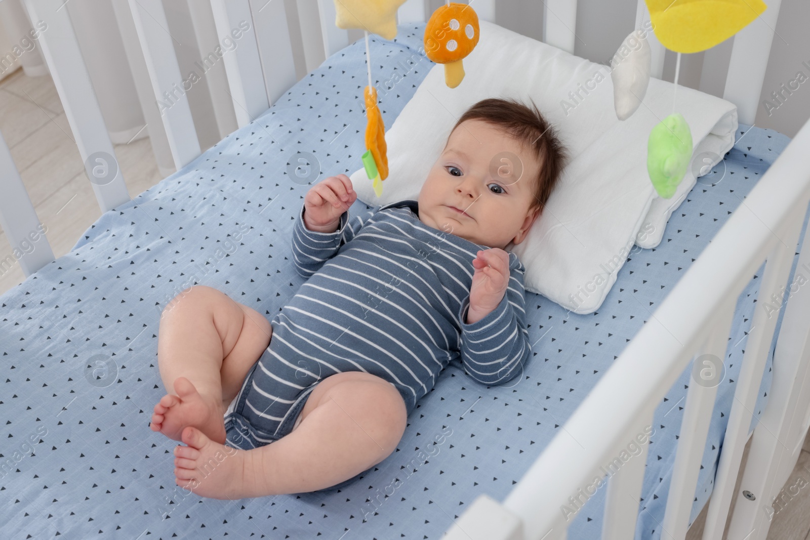 Photo of Cute little baby in crib with cot mobile at home