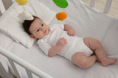 Photo of Cute little baby in crib with cot mobile at home