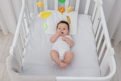 Photo of Cute little baby in crib with cot mobile at home