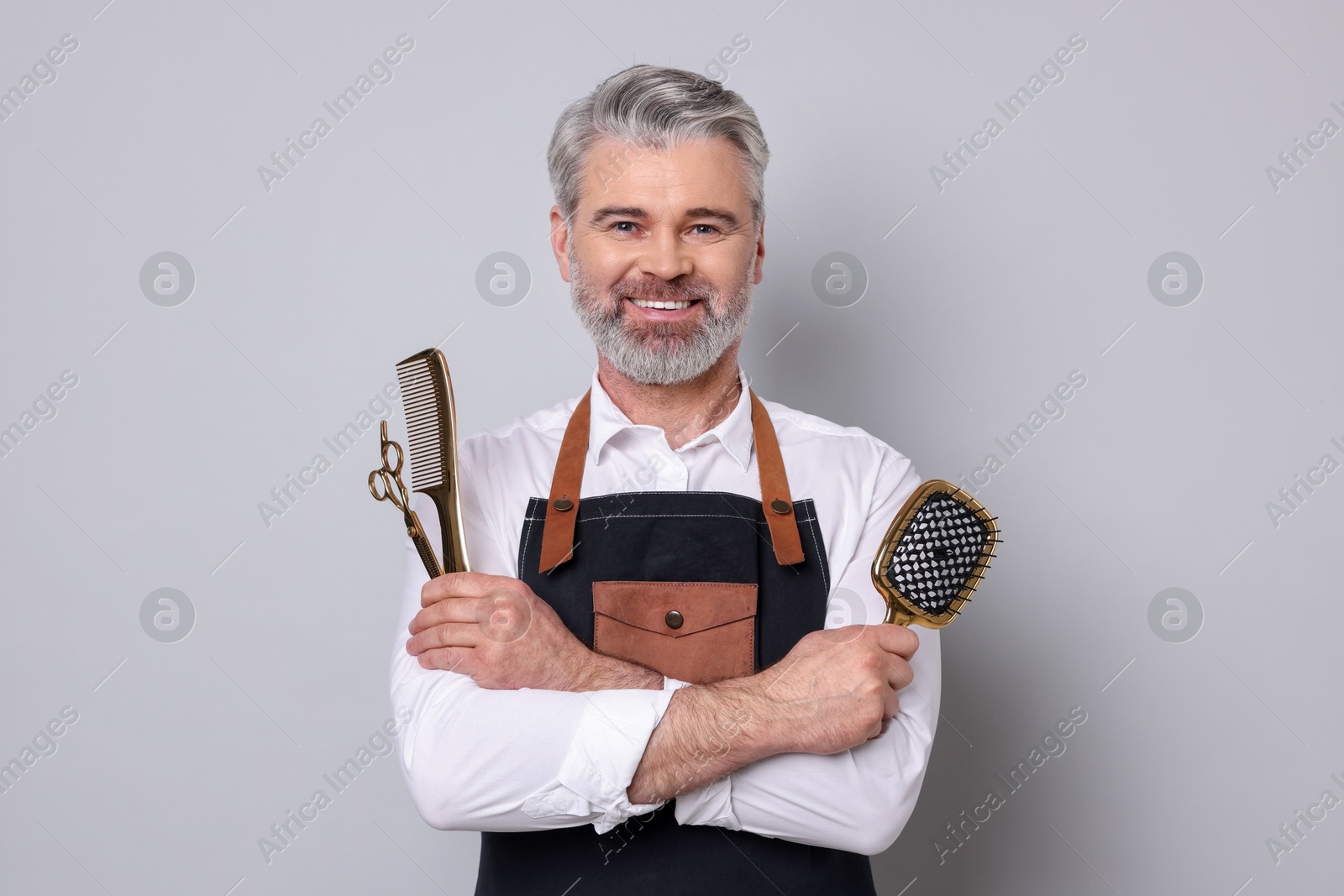 Photo of Smiling hairdresser with scissors, comb and brush on gray background