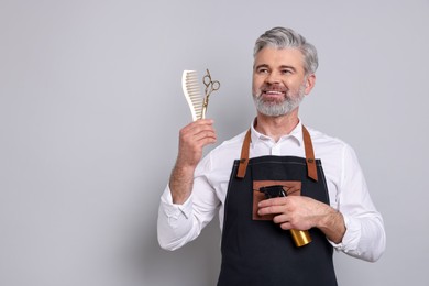 Smiling hairdresser with scissors, comb and spray bottle on gray background, space for text