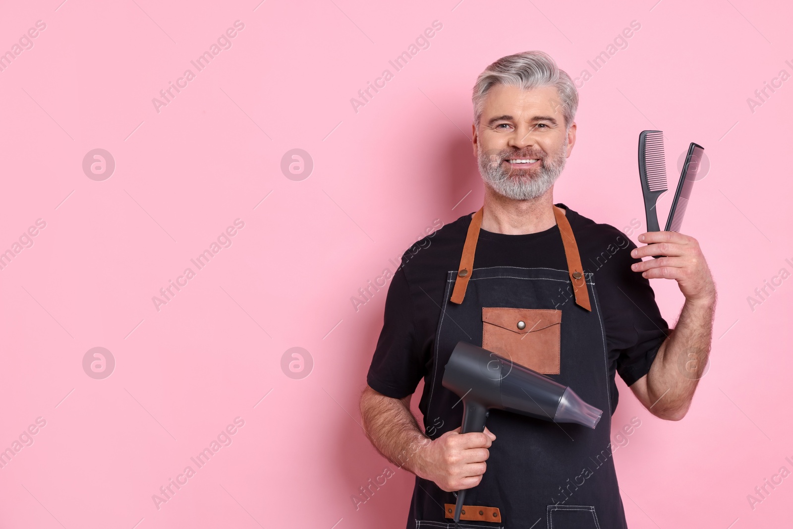 Photo of Smiling hairdresser with dryer and combs on pink background, space for text