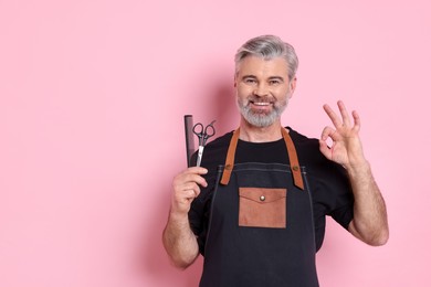 Photo of Smiling hairdresser with scissors and comb showing OK gesture on pink background, space for text