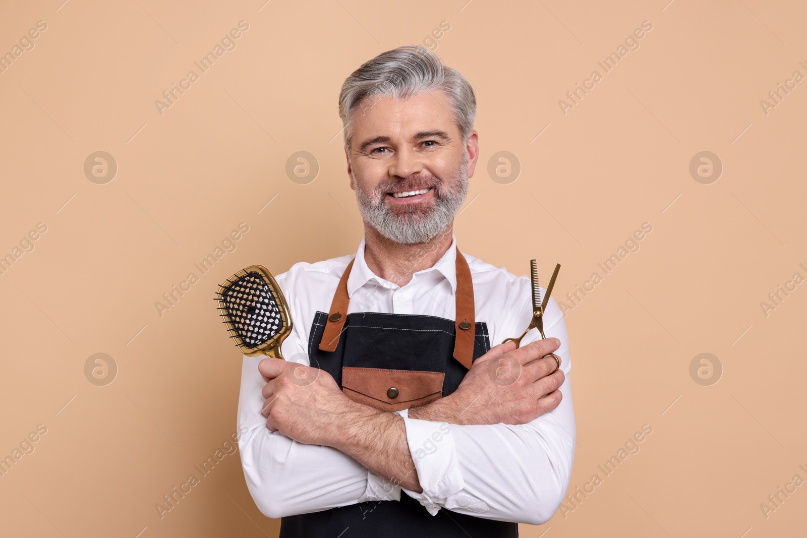 Photo of Smiling hairdresser with scissors and brush on beige background