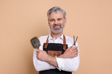 Photo of Smiling hairdresser with scissors and brush on beige background