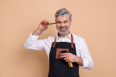 Smiling hairdresser with scissors and spray bottle on beige background