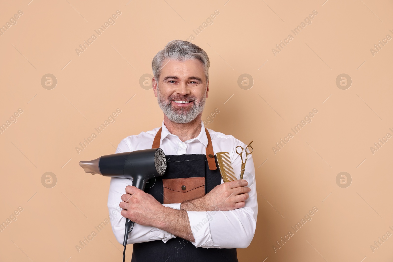 Photo of Smiling hairdresser with dryer, scissors and comb on beige background