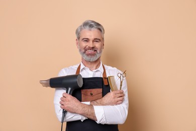 Smiling hairdresser with dryer, scissors and comb on beige background