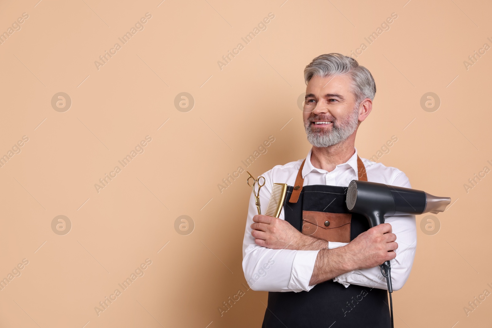 Photo of Smiling hairdresser with dryer, scissors and comb on beige background, space for text