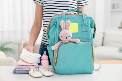 Photo of Mother packing baby's stuff into bag at white table, closeup