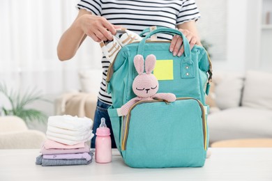 Photo of Mother packing baby's stuff into bag at white table, closeup