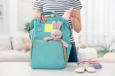 Photo of Mother packing baby's stuff into bag at white table, closeup