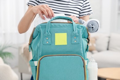 Mother packing baby's stuff into bag indoors, closeup