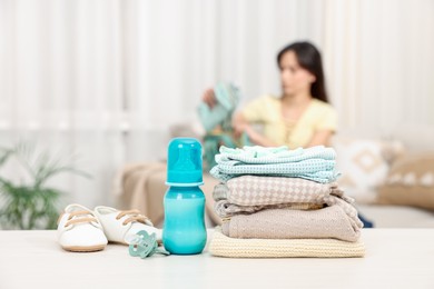 Photo of Baby's stuff on white table and mother packing bag, selective focus